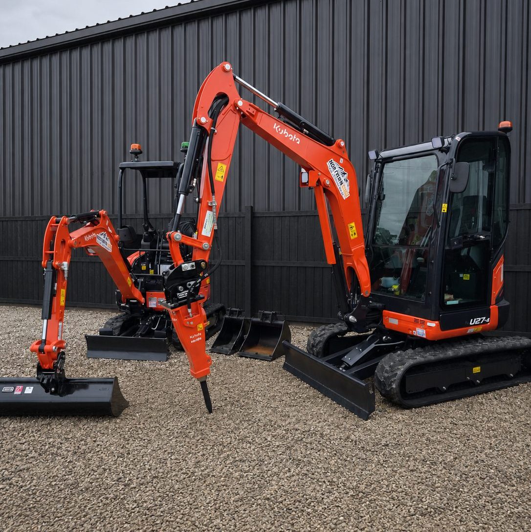 Kubota U17-5 and U27-4 mini excavators parked with their attachments against dark yard cladding
