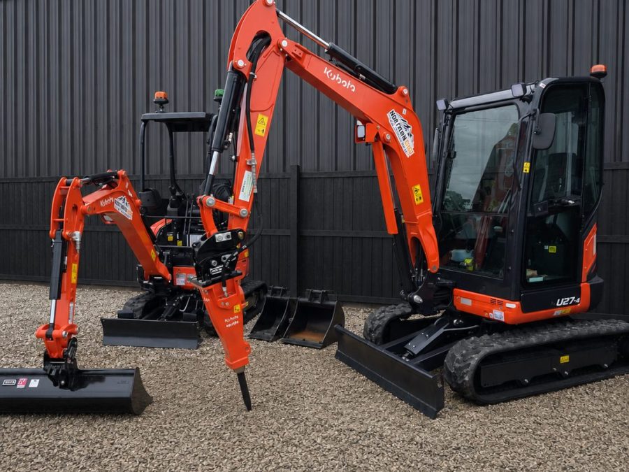 Kubota U17-5 and U27-4 mini excavators parked with their attachments against dark yard cladding